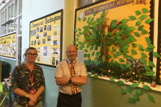 Two teachers standing next to a tree artwork created by pupils 