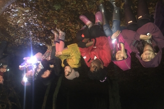 Primary school children sitting on a log in the dark holding torches 