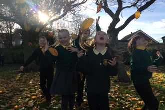 Group of pupils laughing as they throw leaves in the air