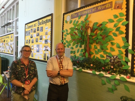 Two teachers standing next to a tree artwork created by pupils 