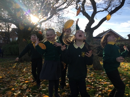 Group of pupils laughing as they throw leaves in the air